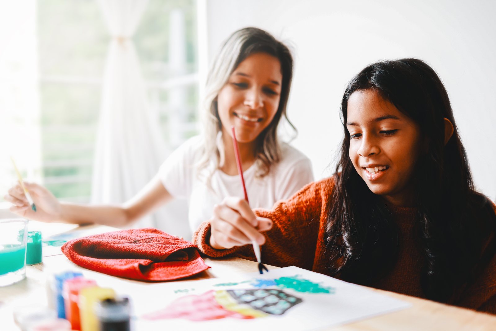 A mother and daughter paint together at the table, smiling