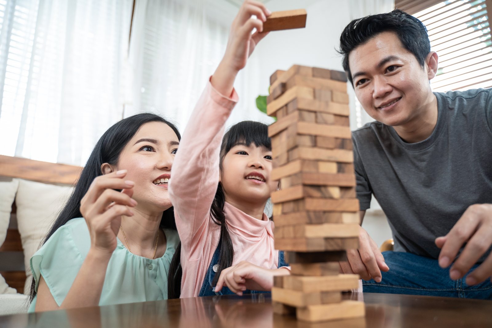 A mother, father, and daughter build a wooden block tower together at their kitchen table